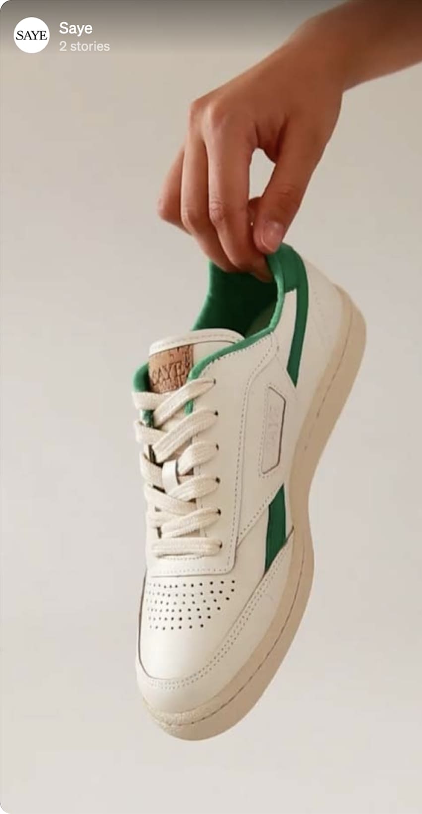 Footwear ad — a hand holding a white-and-green sneaker